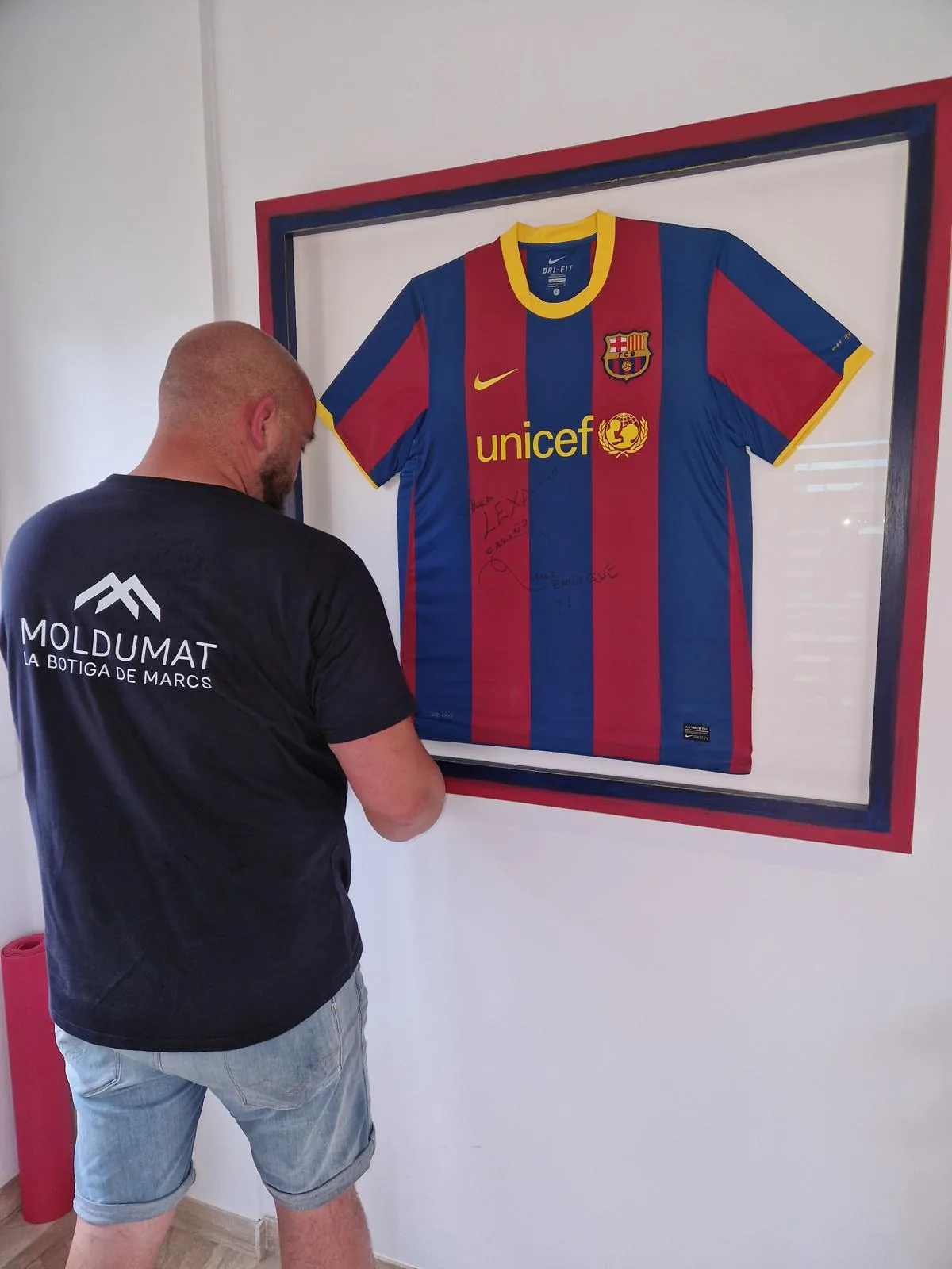 Camiseta firmada del FC Barcelona enmarcada en una vitrina azul y granate, recién colgada en casa del cliente