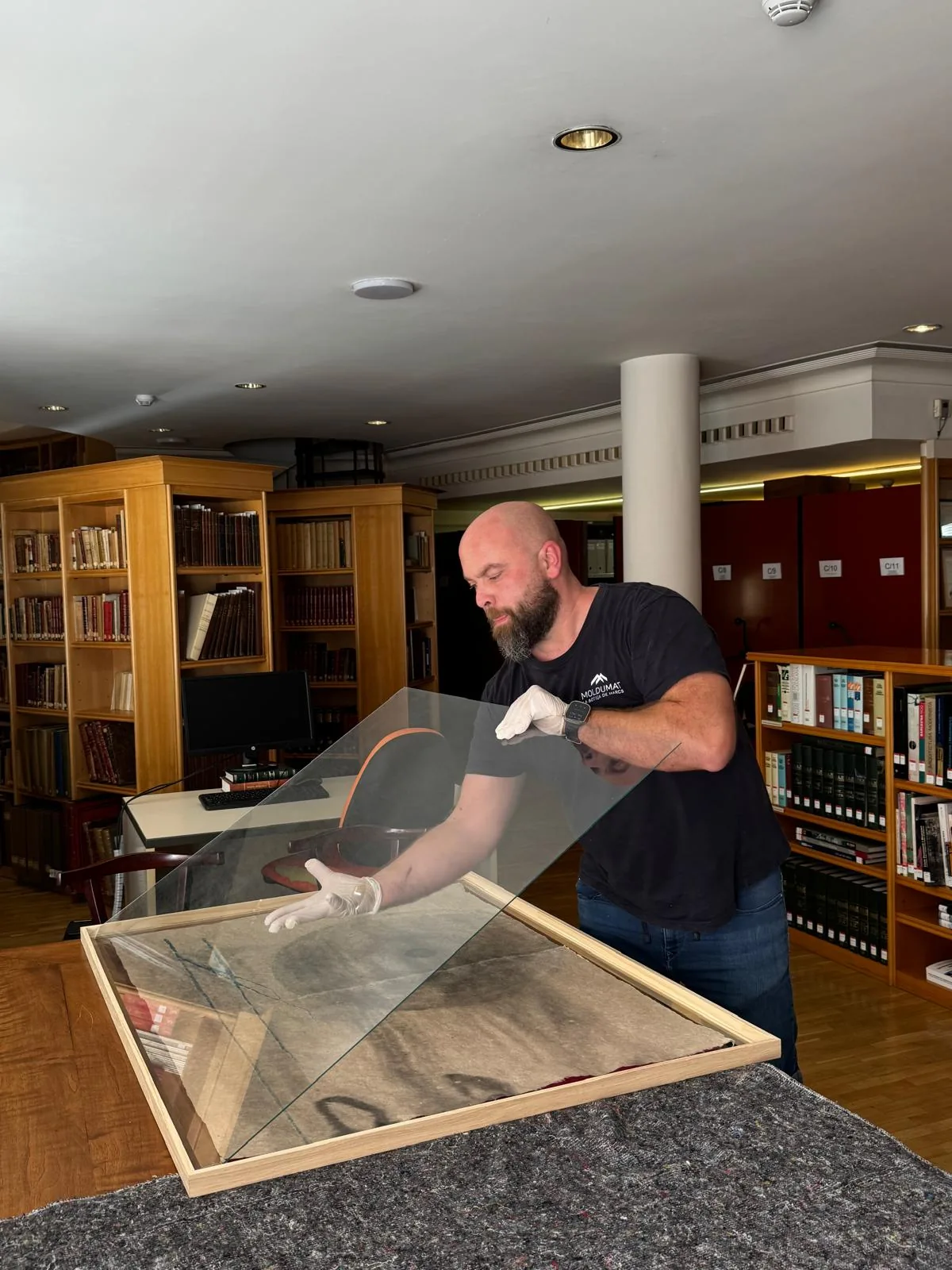 Operario de Moldumat colocando con guantes el cristal sobre una obra, en la biblioteca de una institución