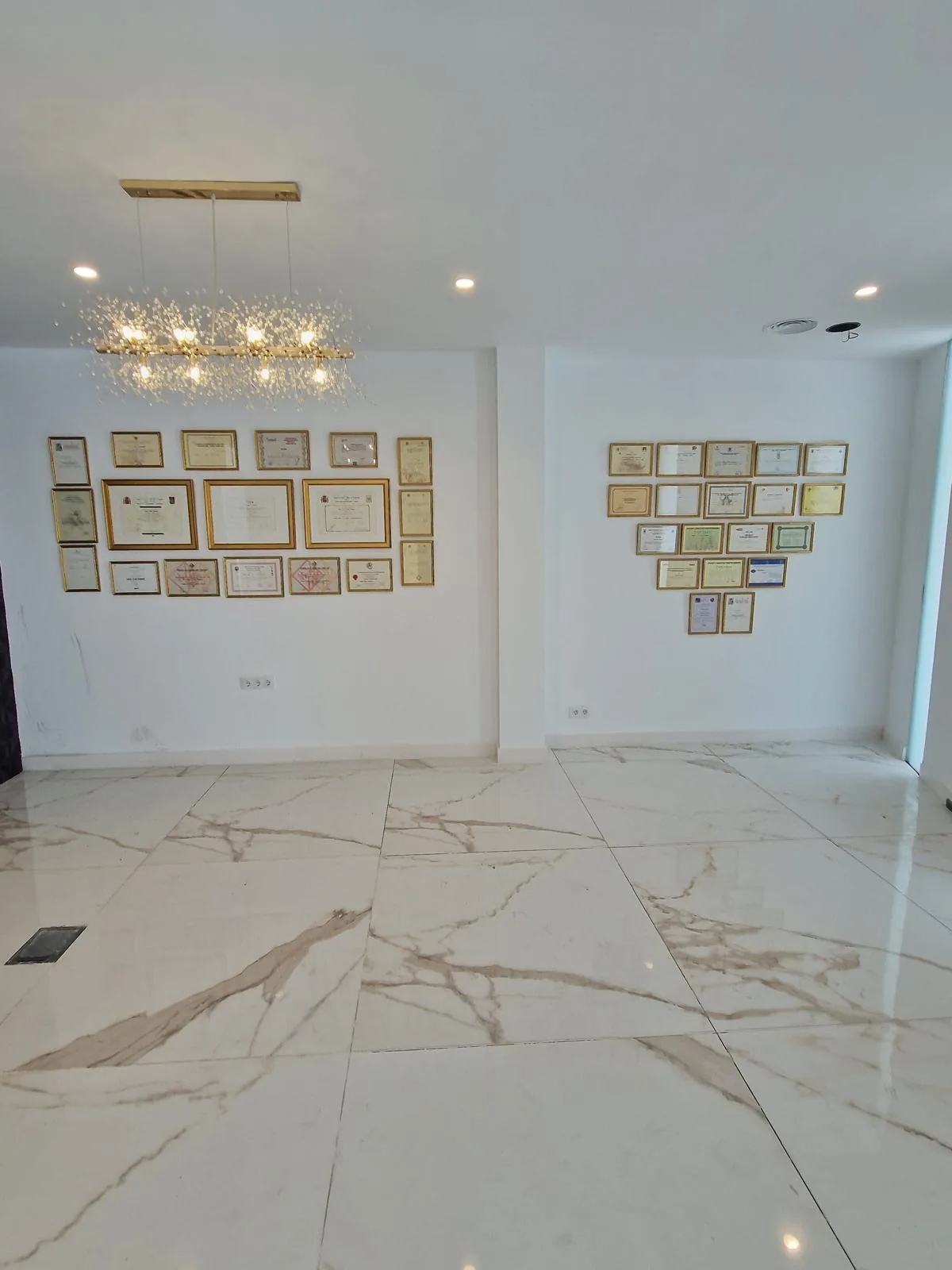 Dos composiciones de diplomas y certificados enmarcados en la pared de una sala amplia