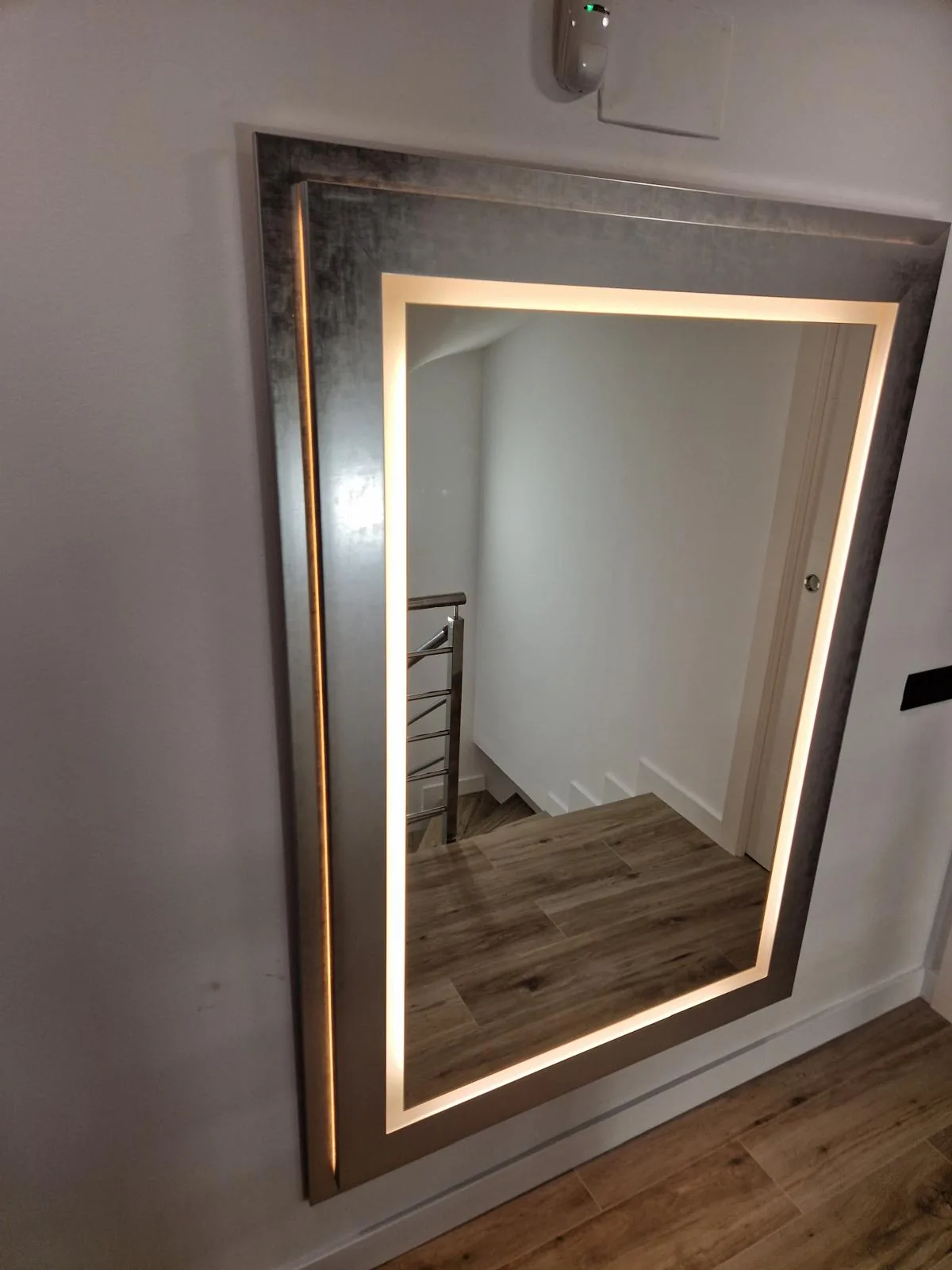 Espejo a medida con marco de madera envejecida y luz LED perimetral, colgado en el recibidor de una vivienda