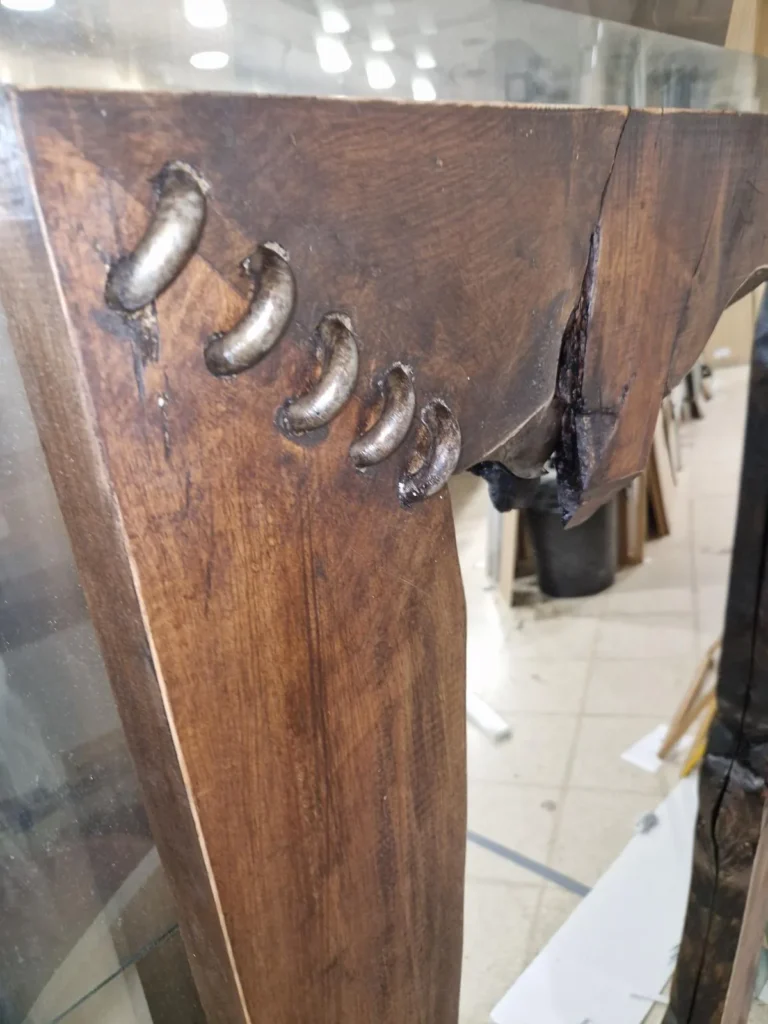 Detalle de un marco de madera maciza de borde vivo, con grapas metálicas que cosen una grieta de la madera
