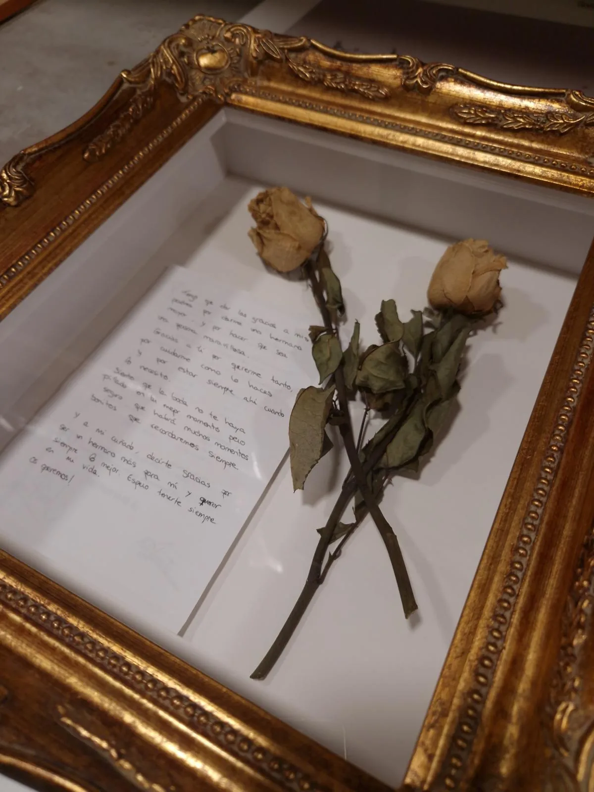 Dos rosas secas y una carta manuscrita montadas con volumen dentro de un marco dorado