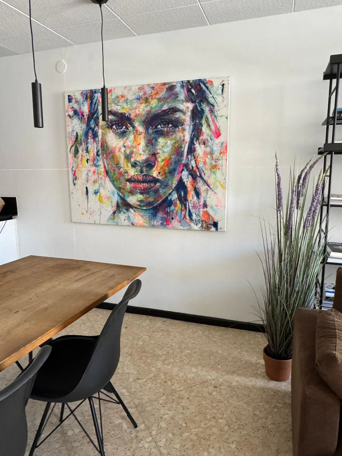 Retrato sobre lienzo enmarcado al canto, colgado en una sala con mesa de madera