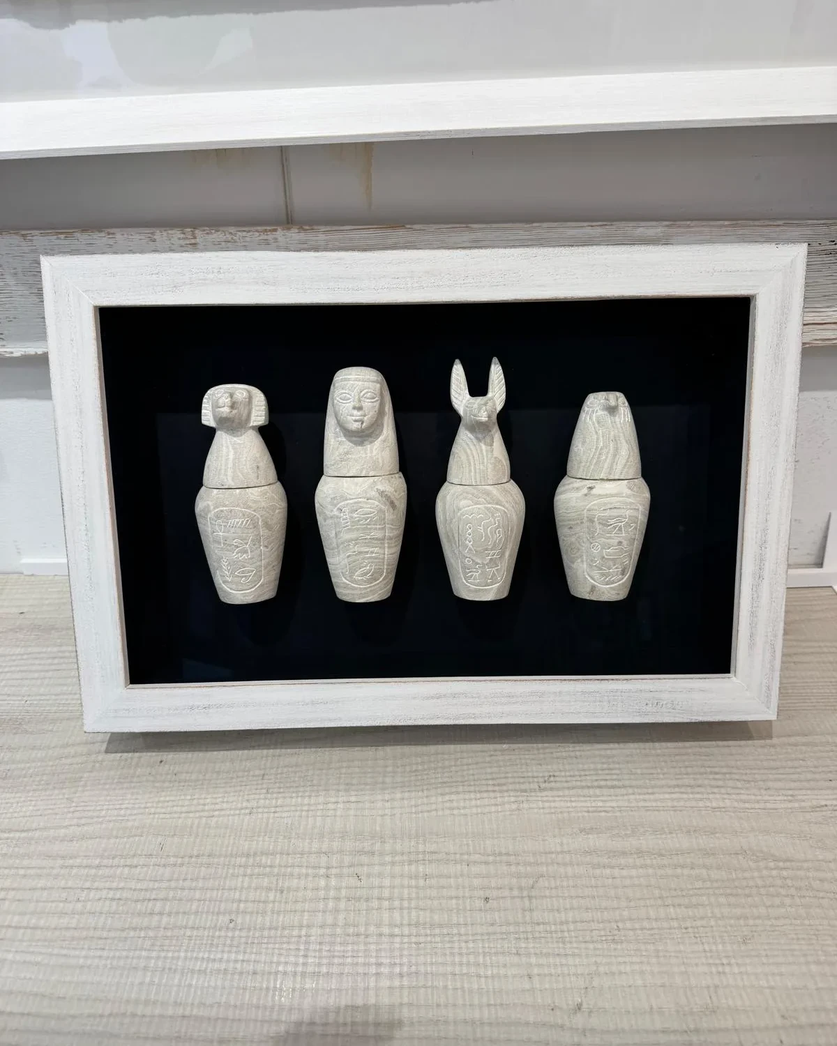 Cuatro vasos canopos egipcios montados sobre fondo negro en una vitrina de marco blanco envejecido