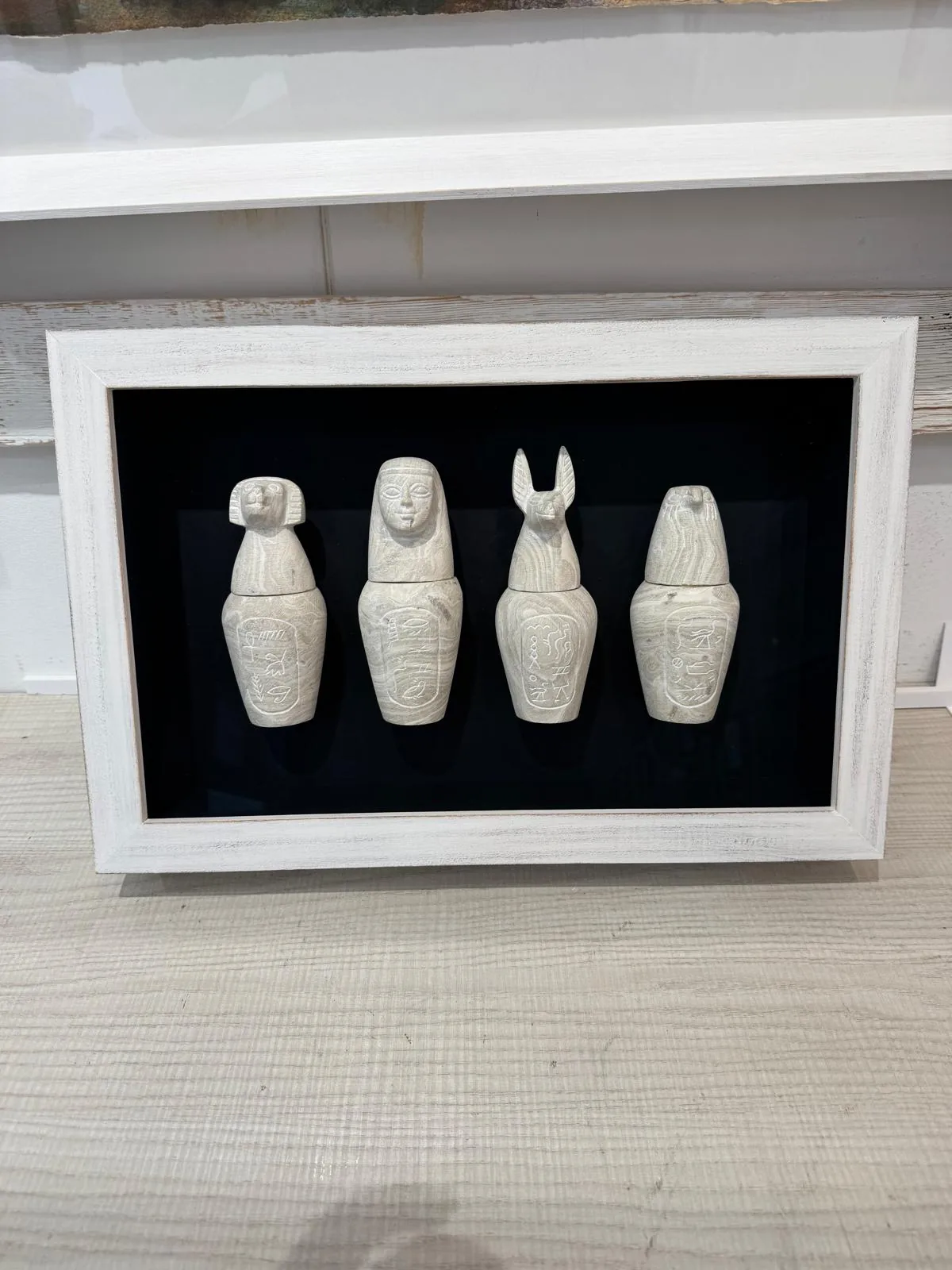 Cuatro vasos canopos egipcios montados sobre fondo negro en una vitrina de marco blanco envejecido