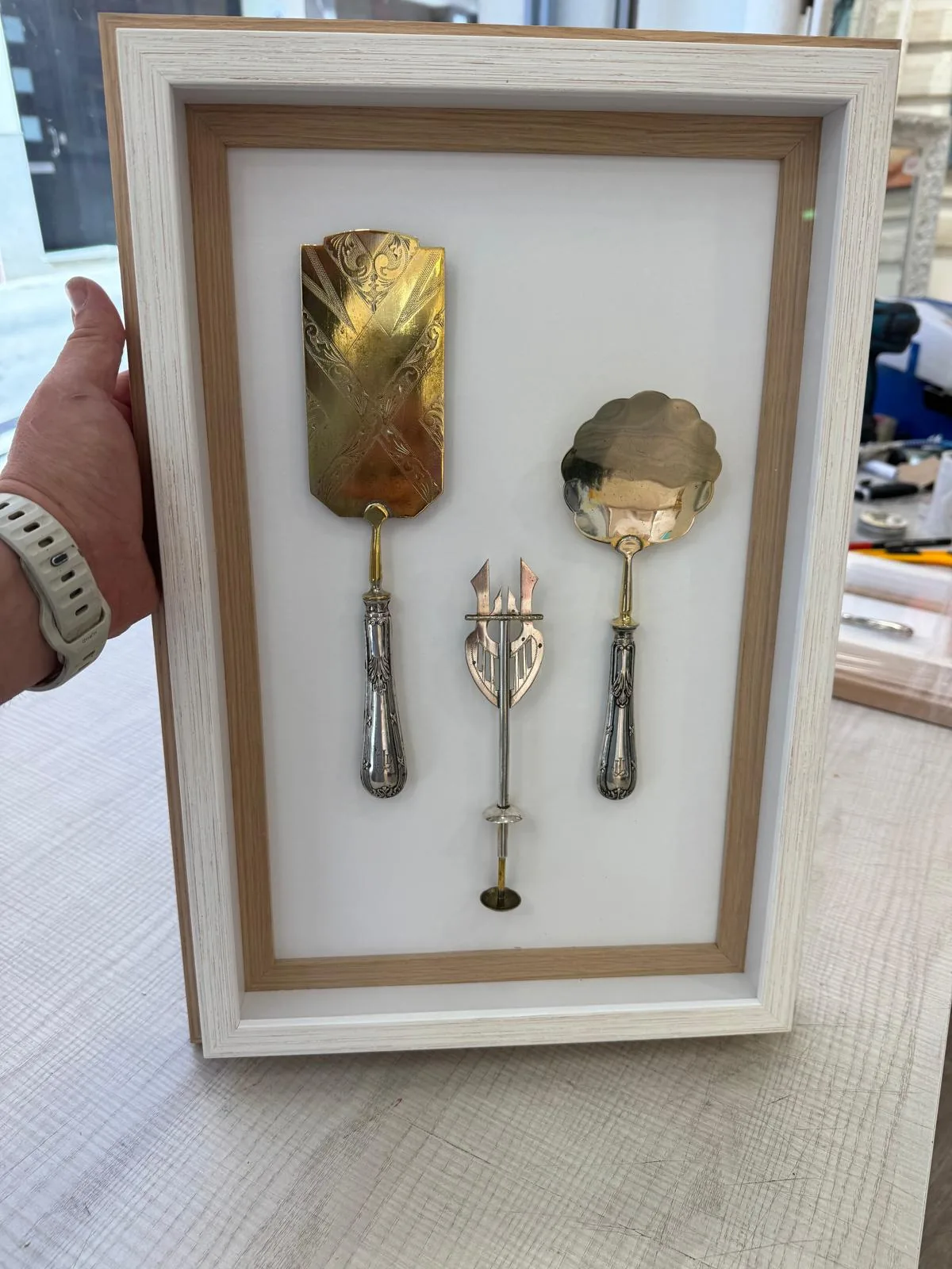Cubiertos antiguos de plata y bronce montados sobre fondo blanco en una vitrina de madera clara