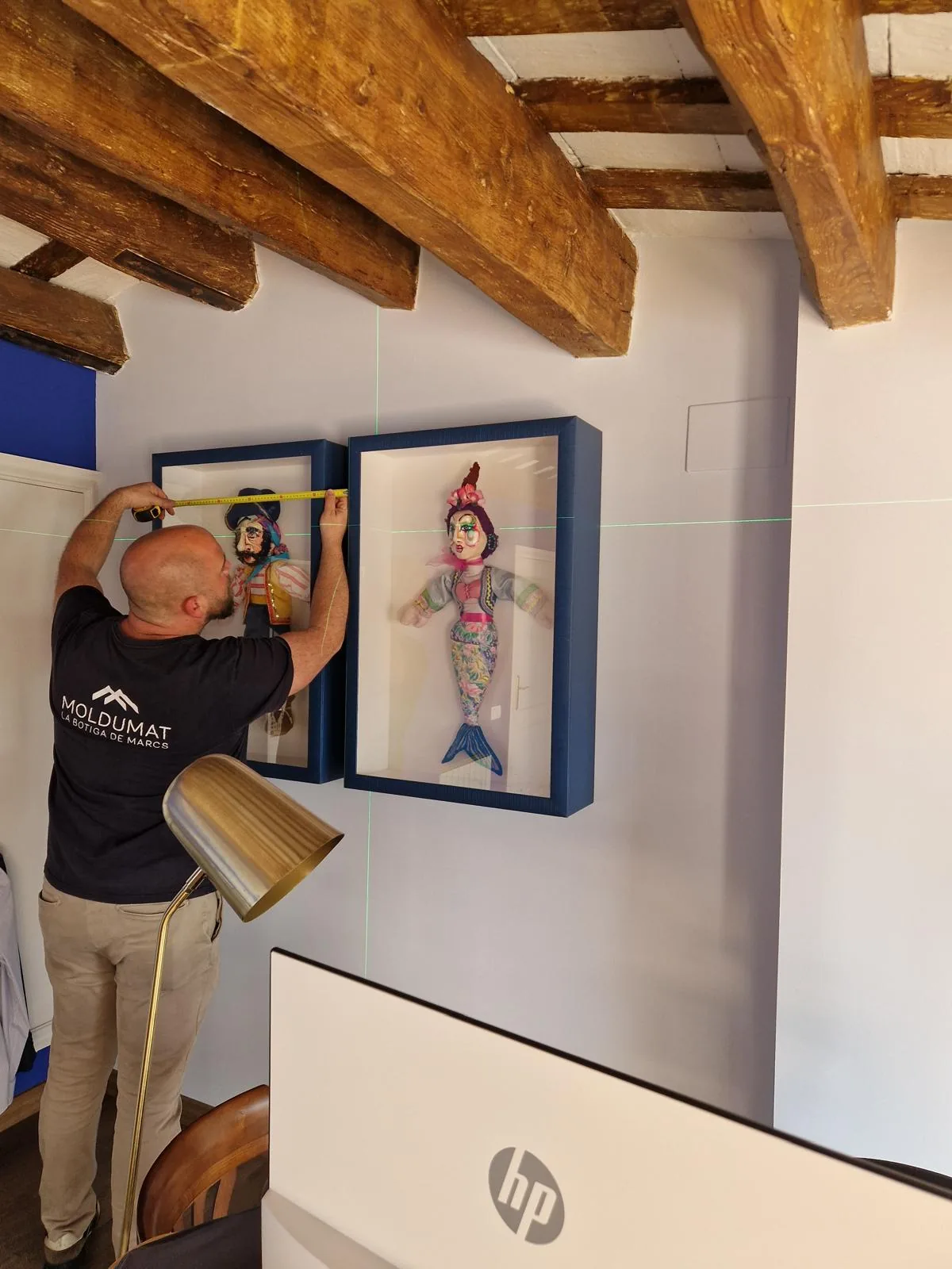 Operario de Moldumat midiendo la colocación de dos vitrinas azules con marionetas en la pared del cliente